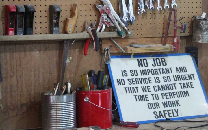 A sign rests on a wall against tools. It reads "No job is so important and no service is so urgent that we cannot take time to perform our work safely."